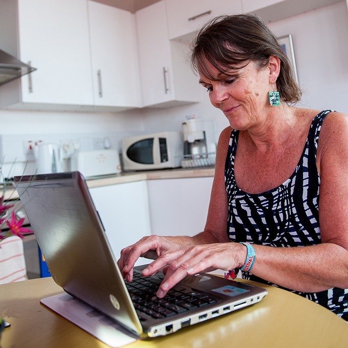 Person sitting down using a laptop with kitchen appliances in the background