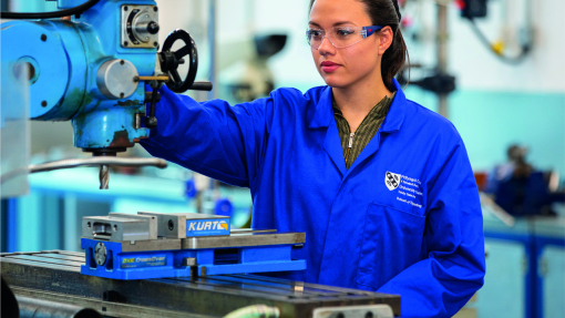 Apprentice working machinery wearing blue overalls