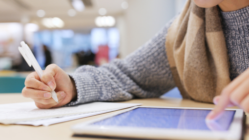 Student working on a tablet and writing on a notepad
