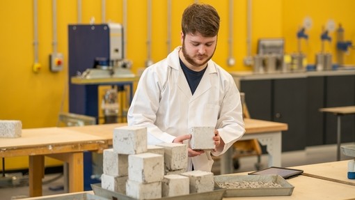 Student in lab coat holding a cube structure