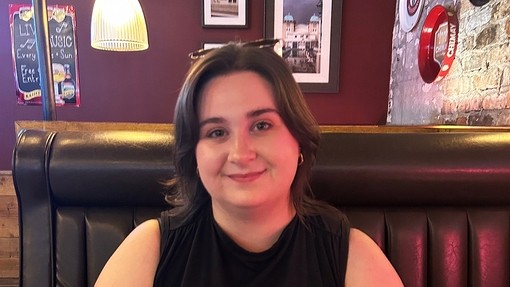 Rebecca Hodgson sits in a booth in a bar and smiles towards the camera.