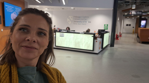 Woman taking selfie in front of glass reception desk at UWTSD's IQ building