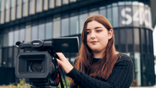 woman standing behind camera in front of building that says S4C