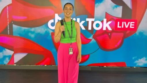 woman holding a microphone in front of backdrop that's branded 'TikTok Live'