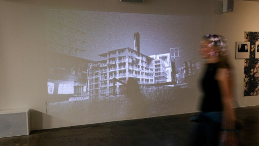 A building is projected onto a wall and an out of focus student is walking past the exhibition.