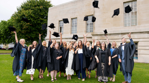 a group of the students outside the Brangwyn Hall throwing caps