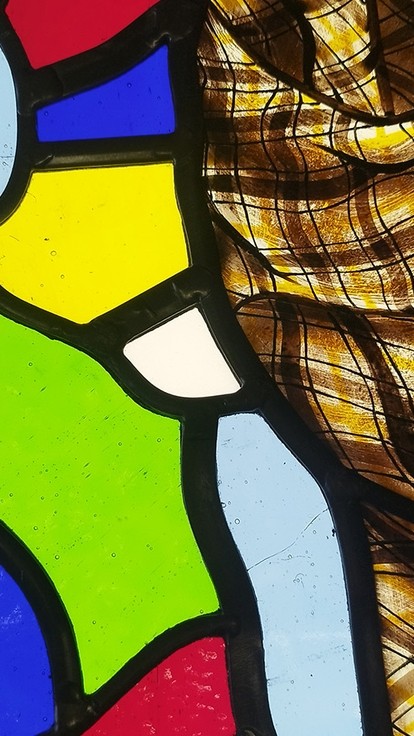 Pieces of stained glass in primary colours divided by black cames; half the glass is covered by a thin piece of chequered cloth. 