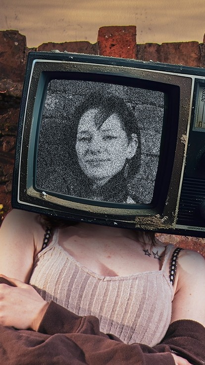 A woman leans against an old brick wall with an old-fashioned TV covering her head; a fuzzy grey image on the screen shows the face of a woman looking calmly out towards the viewer.    