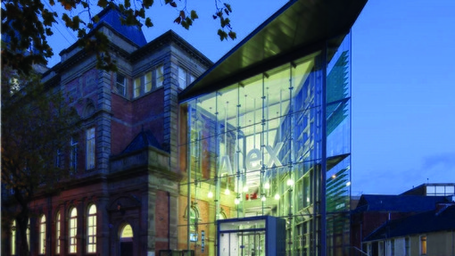 Image of UWTSD Alex building with a glass entrance with ALEX in white letters at dusk