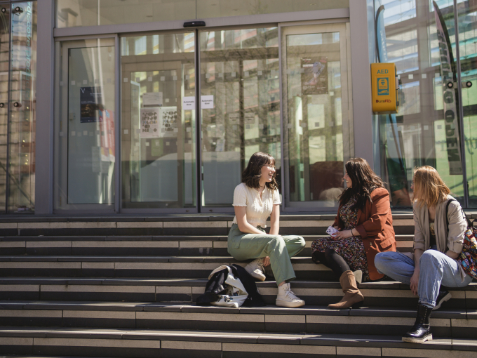 Three students sitting on the steps outside the Alex building