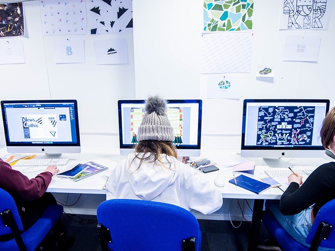 Three students creating designs on Apple Mac computers.