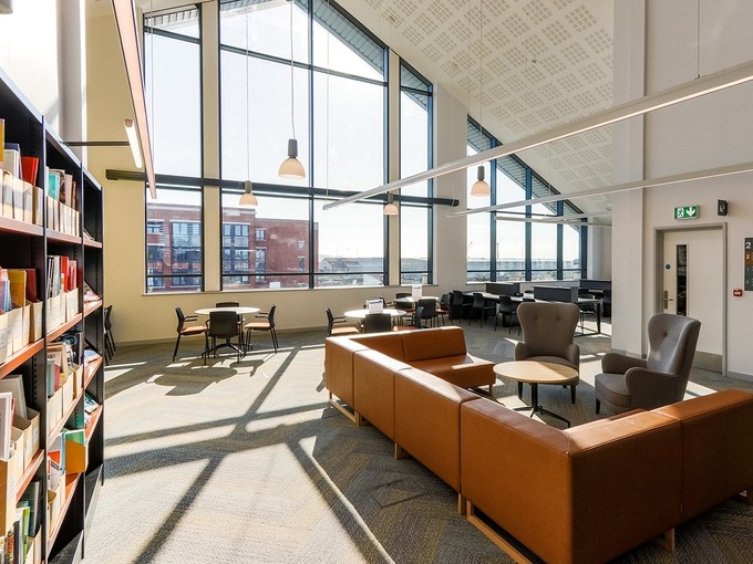 A couch and bookshelves on the top floor of the Fforwm Library; a window occupies the whole wall and light floods in.