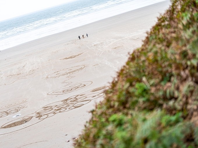 View across Rhossili beach towards three figures drawing lines in the sand.