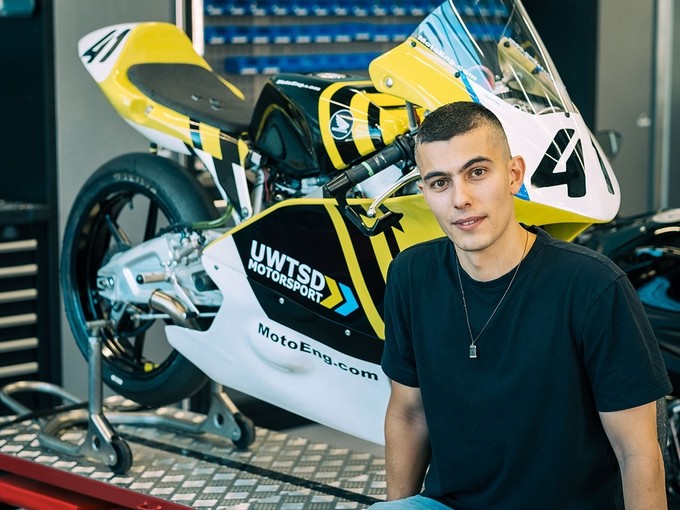 Vinicius Dreher sitting on a platform in front of a UWTSD racing motorbike.