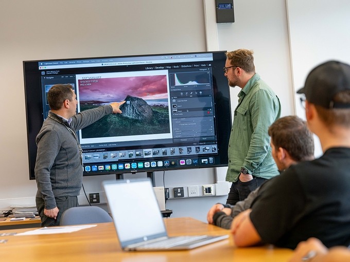 Brett Aggersberg points out a detail on a super-sized monitor displaying a photo of an ancient thatched house in Adobe Lightroom Classic.