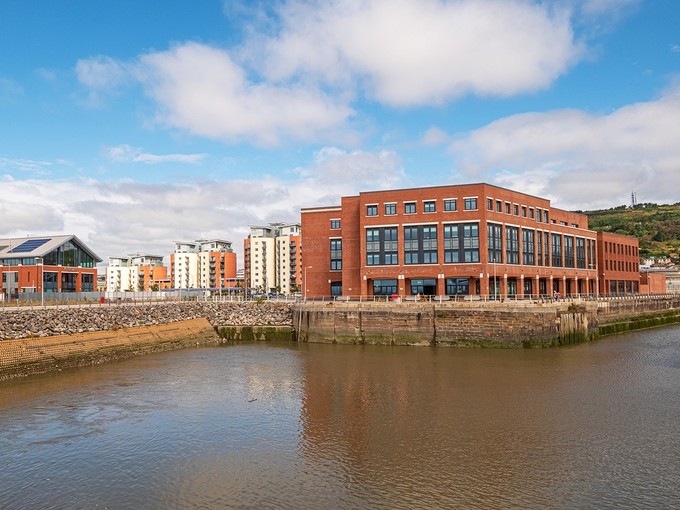View across the flooded Prince of Wales dry dock towards the IQ Building, Fforwm Library, and three blocks of modern flats.