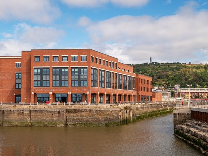 The flooded dry dock and the red-brick IQ Building in the foreground; the wooded slope of Kilvey Hill occupies the background.