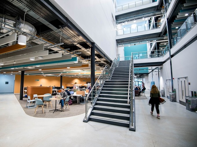 The main lobby of the IQ building; a flight of stairs run up to a first-floor gallery; two further galleries can be seen on the upper storeys; on the ground floor students sit and tables using computers and laptops.
