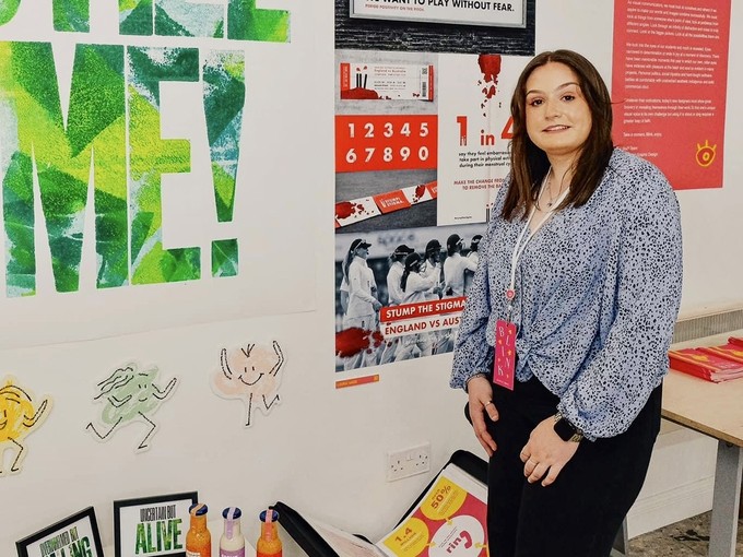 Laura Wade stands next to a white wall covered in prints and posters.