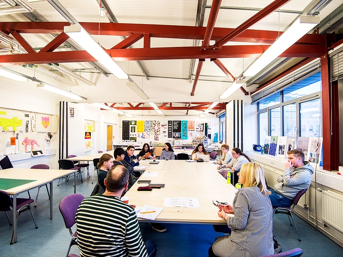 Eleven people sit round a table talking in a high-ceilinged art classroom.