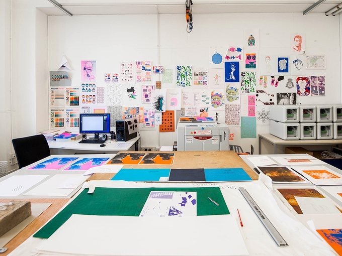 A classroom with a table and walls covered in colourful prints.