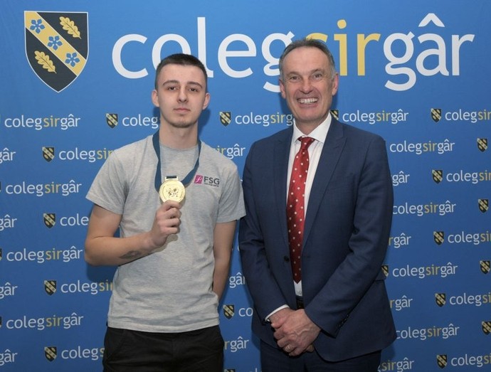 Student Jacob Gibbins proudly wearing a gold medal stands beside the Deputy Vice Chancellor Dylan Jones, celebrating his competition win.