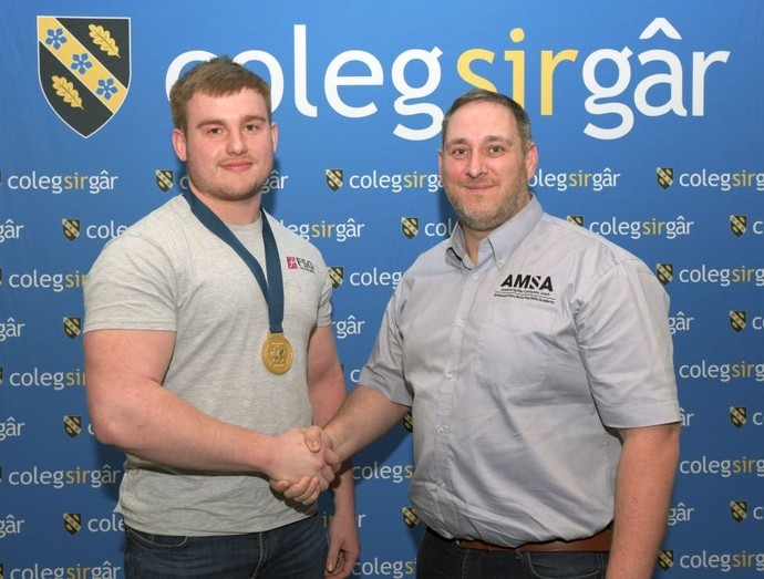 Student Kian Lloyd proudly wearing a gold medal shakes hands with a representative from AMSA (Advanced Manufacturing Skills Academy), celebrating his competition win.