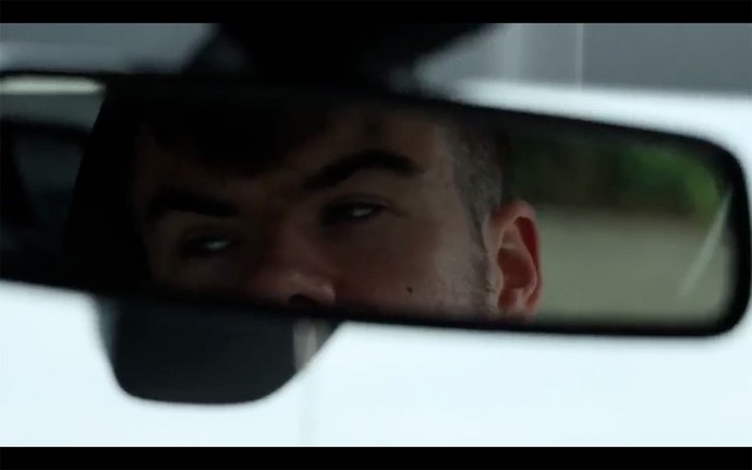 A rear view mirror shows part of the face of a young man as he looks aside towards somethng off-camera.