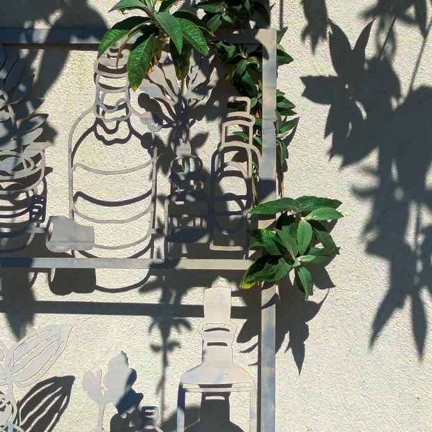 A metal frame supporting small plants in its top corner; the crossbars of the frame support the outlines of metal bottles and containers as if they were shelves in a kitchen.