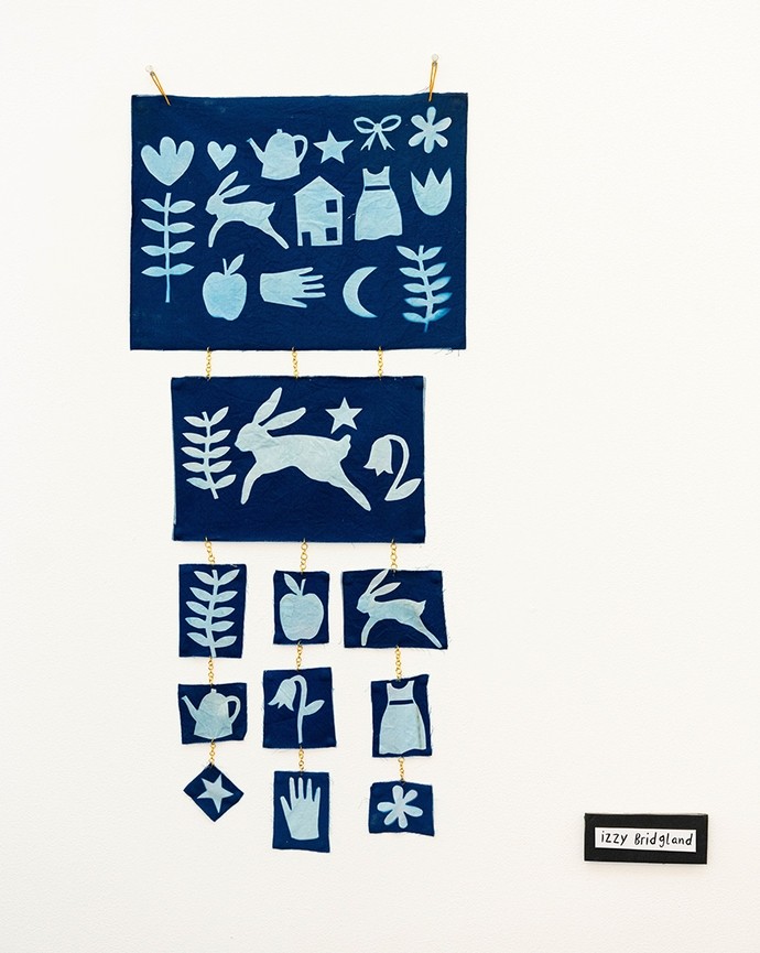 Papercut work in pale blue on dark blue; rectangles display cutouts of hearts, hares, a teapot, a flower and other familiar icons. 