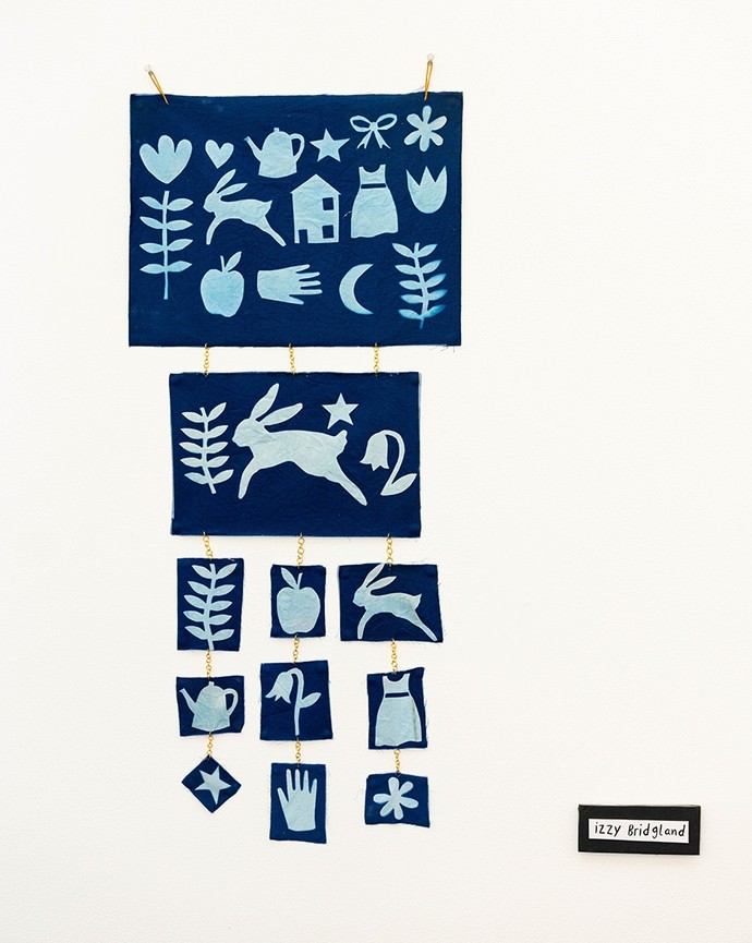 Papercut work in pale blue on dark blue; rectangles display cutouts of hearts, hares, a teapot, a flower and other familiar icons.