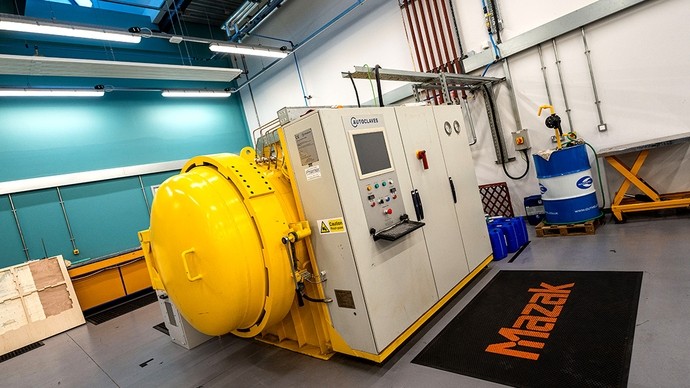 A large autoclave about as tall as a man; a yellow cylindrical chamber projects outwards from behind the grey control cabinet. 