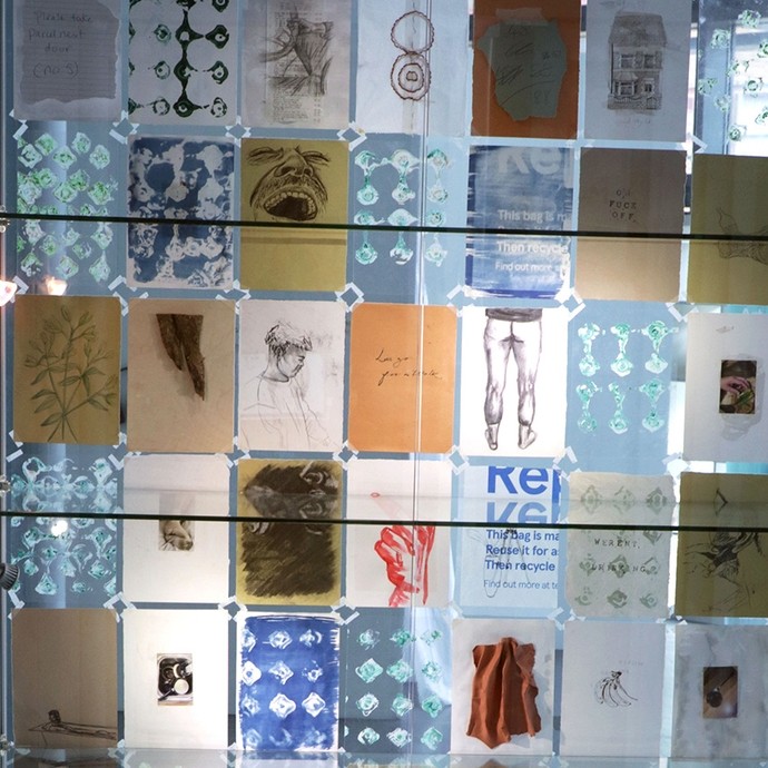 Forty-six postcard-sized pieces of card, each with a different design, displayed in eight vertical rows in a glass cabinet. 