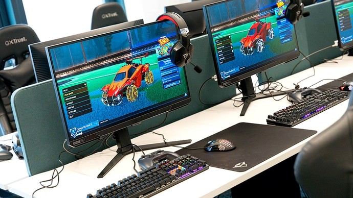 Large monitors showing a colourful computer game interface with a menu and a design for an orange monster truck. 