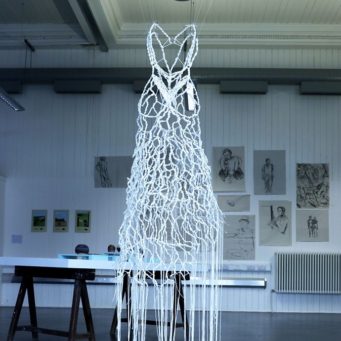 A net of woven white wires in the approximate shape of a dress; it is suspended from the ceiling by thin cables. 