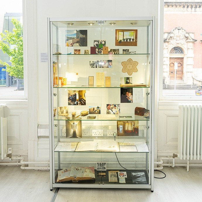 An illuminated glass cabinet full of photos, old documents, spectacles, a small wooden chest, and other items that seem related to the history of a family.