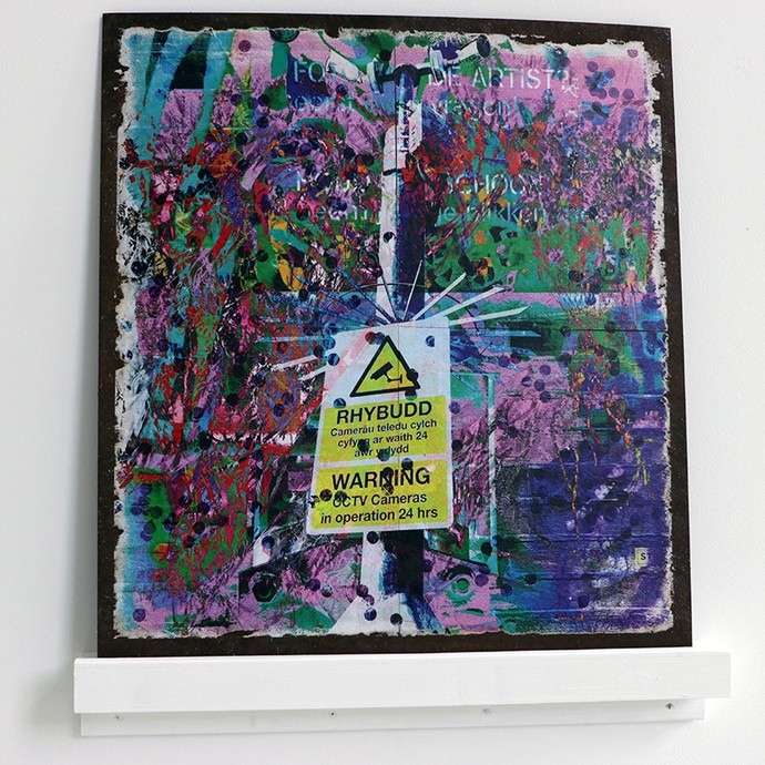 A square canvas covered in smears and dots of paint in green, pink, yellow, turquoise and black; a Welsh and English warning sign in the middle reads Warning: CCTV cameras in operation 24 hours.