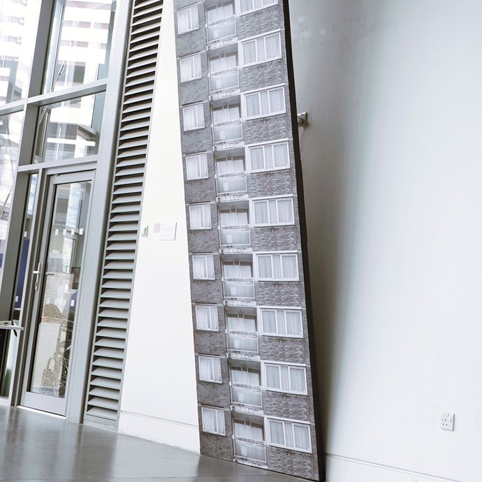 A long narrow photographic work suspended at a 15 degree angle from a corridor wall; it shows a fifteen storey flat, with the windows, grey bricks, and balcony on each storey being identical. 