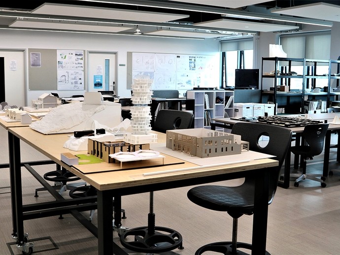 An architecture studio with 3D model buildings spread across the desks; they include a tower build in multiple layers from white card.