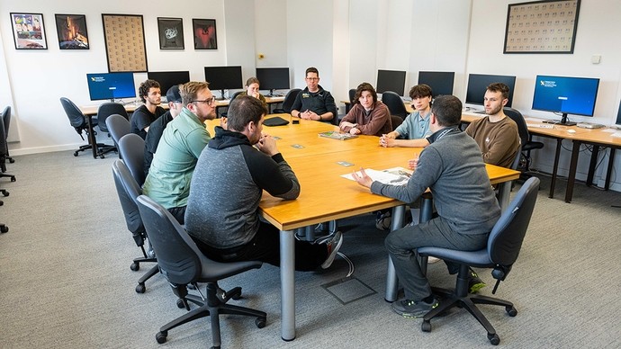 Students sit around a conference table with a lecturer. 