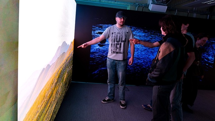 A student points to a mountainous landscape displayed on a digital screen inside the Carmarthen immersive room.