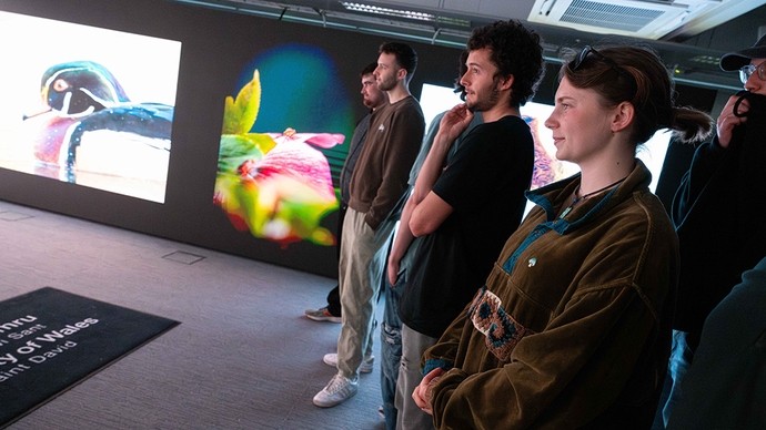 Students stand in the Carmarthen immersive room; one wall displays photos of a male wood duck and an insect on a flower petal. 