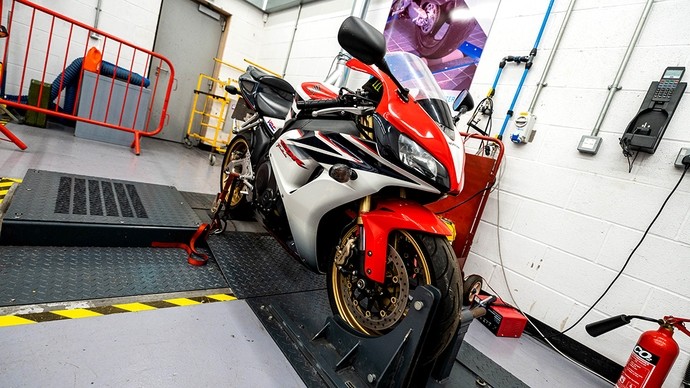 A red-and-silver motorbike in a workshop with its front wheel clamped in a stand. 