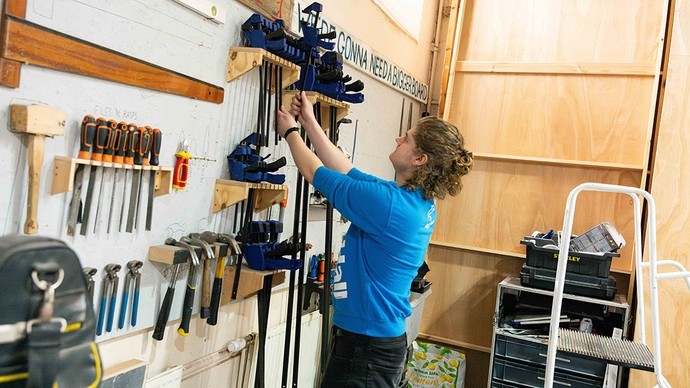 A young man lifts down a wrench from a large tool rack. 