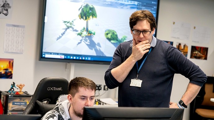 A lecturer holds his chin in his hand as he looks down at the computer screen of a student.