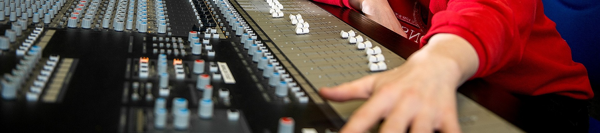 An arm stretches out across a mixing board with numerous sliders and knobs.