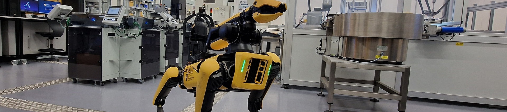 A black and yellow robotic dog standing in a robotics workshop.