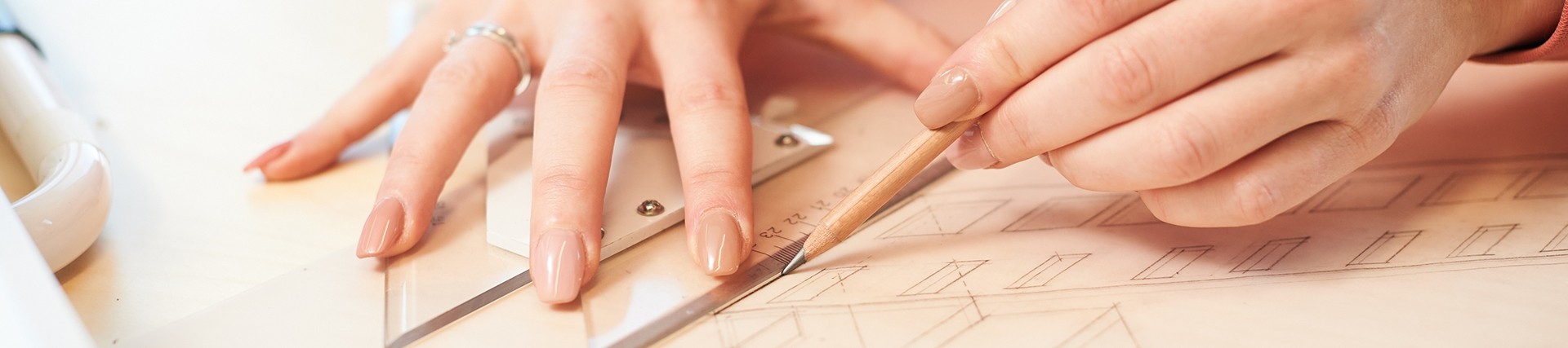 Manicured fingers hold an angle protractor and sharp pencil to draw a line on an architectural design. 