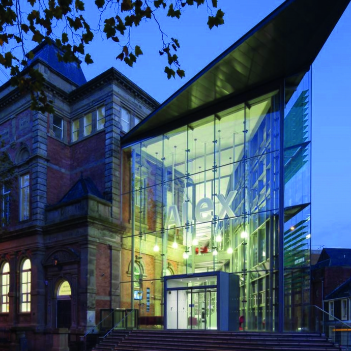 Image of UWTSD Alex building with a glass entrance with ALEX in white letters at dusk