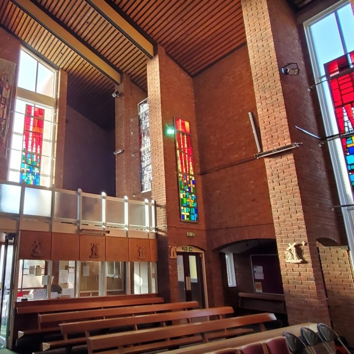 Brick interior of a church with colourful stain glass panels suspended in front of plain windows.